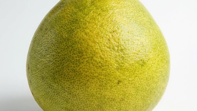A vibrant, fresh citrus fruit, likely a pomelo or large grapefruit, is captured in a detailed close-up shot against a pristine white background. Its distinctive bumpy, textured green-yellow rind showc