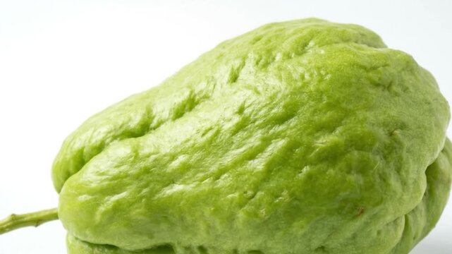 A vibrant, fresh green chayote squash is showcased in a clean, brightly lit studio setting against a pristine white background. The video intimately captures the unique texture of its ridged and sligh
