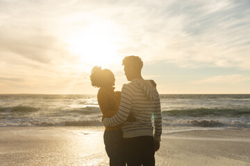 Romantic couple embracing while standing at beach against sky during sunset