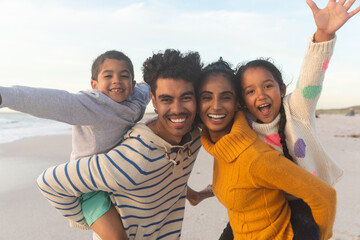 Portrait of happy father and mother giving piggyback rides to kids at beach during sunset
