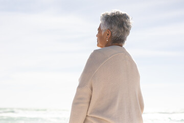 Obraz premium Rear view of retired senior woman looking at sea against sky from beach on sunny day