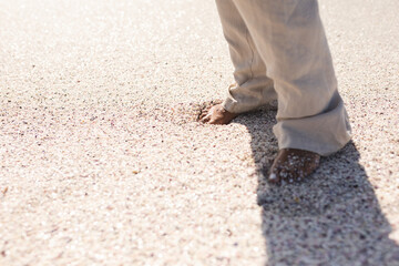 Low section of senior woman standing barefoot on sand at beach during sunny day