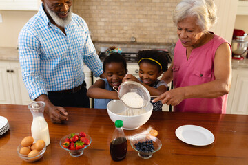 African american grandparents and two granddaughters baking together in the kitchen at home