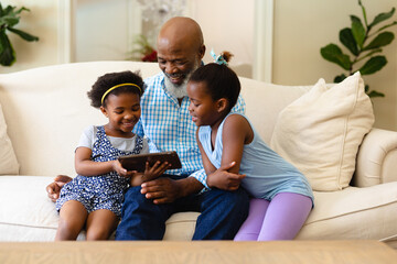 African american grandfather and his two granddaughters using digital tablet at home