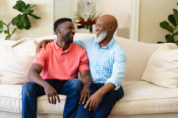 African american father and son smiling looking at each other sitting on couch at home
