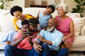African american three generation family using smartphone sitting together on the couch at home