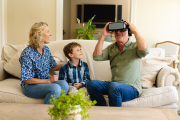 Caucasian grandmother and grandson watching grandfather wearing vr headset sitting on couch at home