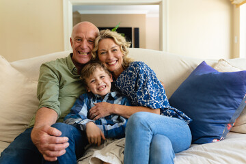 Portrait of caucasian grandparents and grandson smiling while sitting together on the couch at home