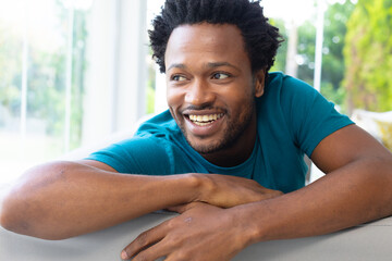 Happy african american young man looking away while sitting on sofa at home