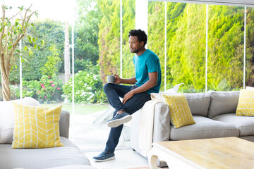 Thoughtful young african american man with coffee mug sitting on sofa in living room at home