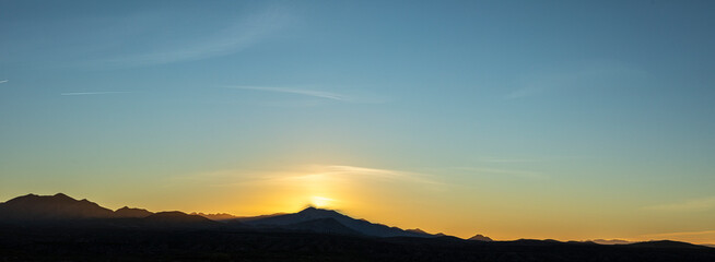 Sun setting behind silhouetted mountain landscape panorama