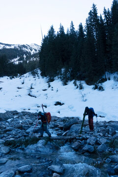 Two skiers cross a river in the Canadian backcountry.
