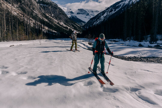Two skiers descend a valley over grizzly tracks.