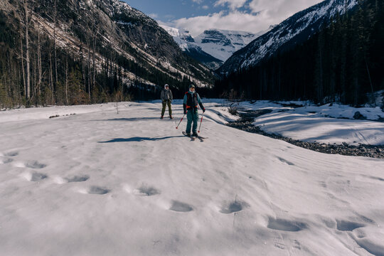 Two skiers descend a valley next to grizzly tracks.
