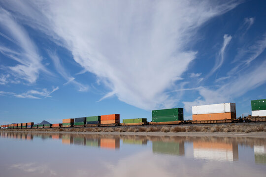 Container stack train reflected in standing water under cloudy sky