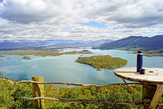 Thermos standing on a wooden viewpoint table overlooking Slano Lake in Montenegro. Symbolizes mindful travel, remote work outdoors, slow tourism, nature immersion, digital detox, and Balkan landscapes