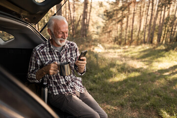 Senior man relaxing checking smartphone outdoors while camping