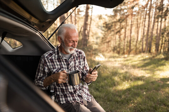 Senior man relaxing in forest using smartphone and drinking coffee - Powered by Adobe