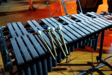 A vibraphone with resting mallets stands on a warmly lit stage, its metal bars and resonators ready for a live orchestral or jazz performance