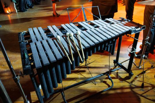 A vibraphone with resting mallets stands on a warmly lit stage, its metal bars and resonators ready for a live orchestral or jazz performance