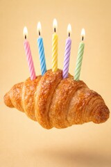 Croissant birthday cake with candles on a tan background for a festive occasion.