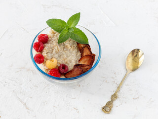 Oatmeal porridge with berries in a glass bowl on the white table.