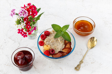 Oatmeal porridge with berries in a glass bowl on the white table.