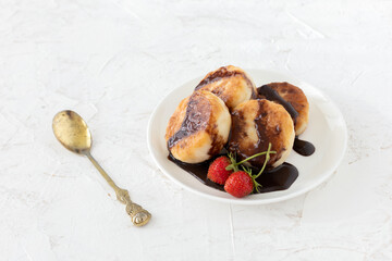 Curd fritters with chocolate and strawberries on the porcelain plate.