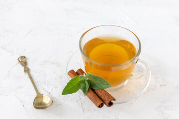 Glass cup of green tea with cinnamon and leaves of mint on a saucer.