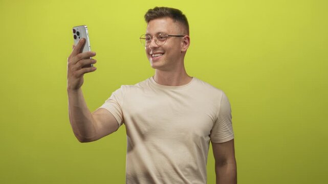Man taking selfie with smartphone, arm extended showing hand and forearm, wearing glasses in studio setting with lime wall; casual confidence.