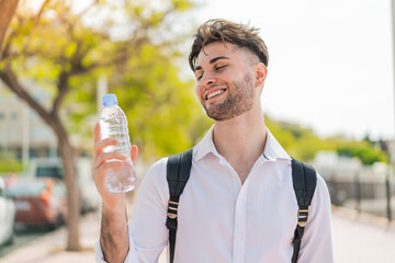 Young handsome man with a bottle of water at outdoors with happy expression
