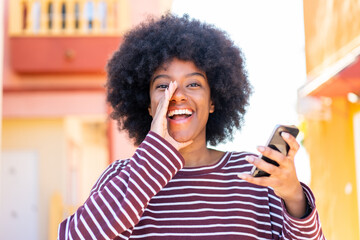 African American girl using mobile phone at outdoors shouting with mouth wide open