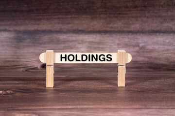 Fototapeta premium Holdings symbol. Clothespins gripping a wooden stick against a beautiful Brown Wooden Background . Business and Holdings concept with copy space