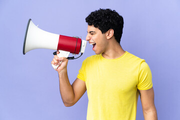 Young Venezuelan man isolated on purple background shouting through a megaphone to announce something in lateral position