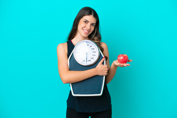 Young Italian woman isolated on blue background with weighing machine and with an apple