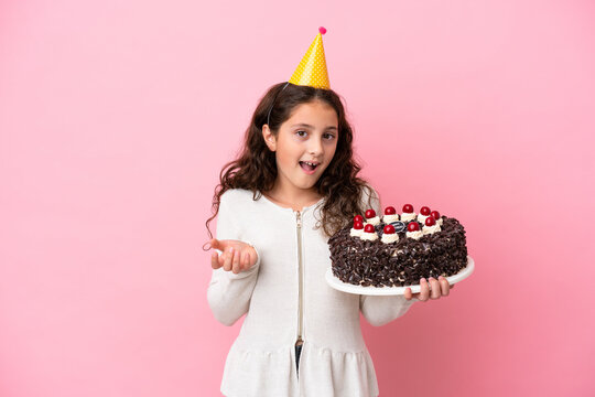 Little caucasian girl holding birthday cake isolated on pink background with shocked facial expression
