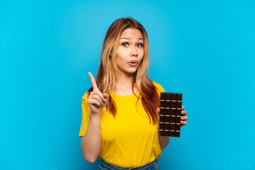 Teenager girl holding chocolat over isolated blue background intending to realizes the solution while lifting a finger up
