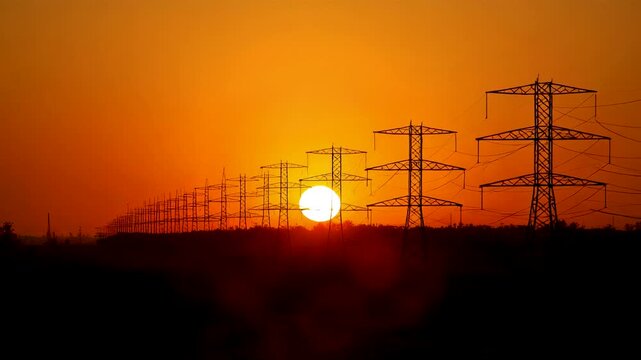 Sunset over electricity pylons and power lines silhouette against orange sky