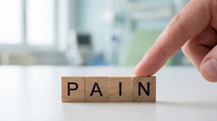 Naklejka premium Mans finger touching wooden blocks spelling PAIN in a bright, modern office setting Concept of chronic pain, discomfort, and medical issues