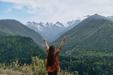 Person standing with arms raised admiring nature and landscape among mountains outdoors, expressing...