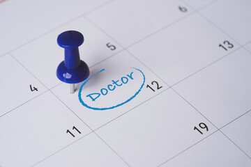 Doctor appointment marked on calendar with blue push pin showing healthcare planning and medical schedule reminder for hospital visit date health check patient care and medical management concept.