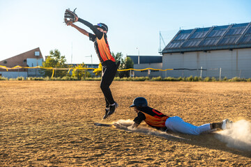 Baseball player sliding into base while field player jumping