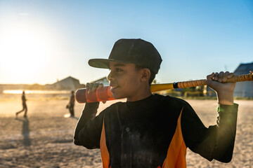 Young boy holding baseball bat on field at sunset