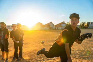 Youth baseball pitcher throwing ball during sunset game