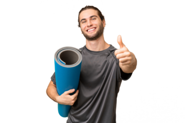 Young sport man going to yoga classes while holding a mat over isolated background with thumbs up because something good has happened