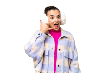 Young woman wearing winter muffs over isolated chroma key background making phone gesture. Call me back sign