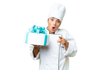 Woman pastry chef with a big cake surprised and pointing front