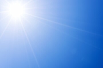 A photograph of the sun shining brightly against a beautiful natural backdrop of a blue sky.