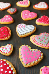 Many of beautiful heart shaped royal icing cookies scattered on black wooden background