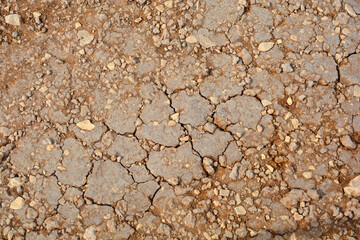 Top down close up view of parched and cracked brown soil with small stones on the ground surface